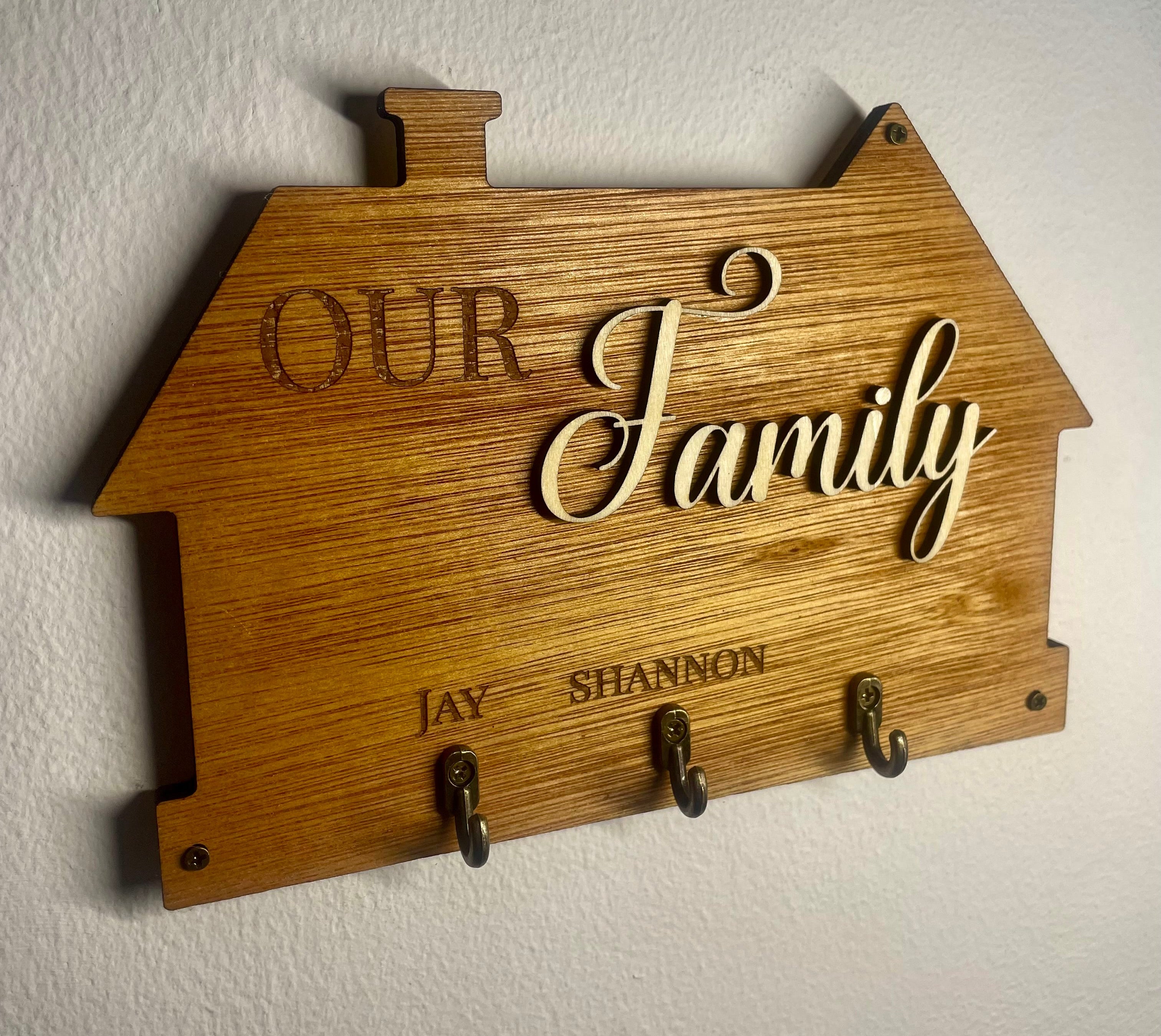 Wooden plaque with 'Our Family' text and hooks on a white wall