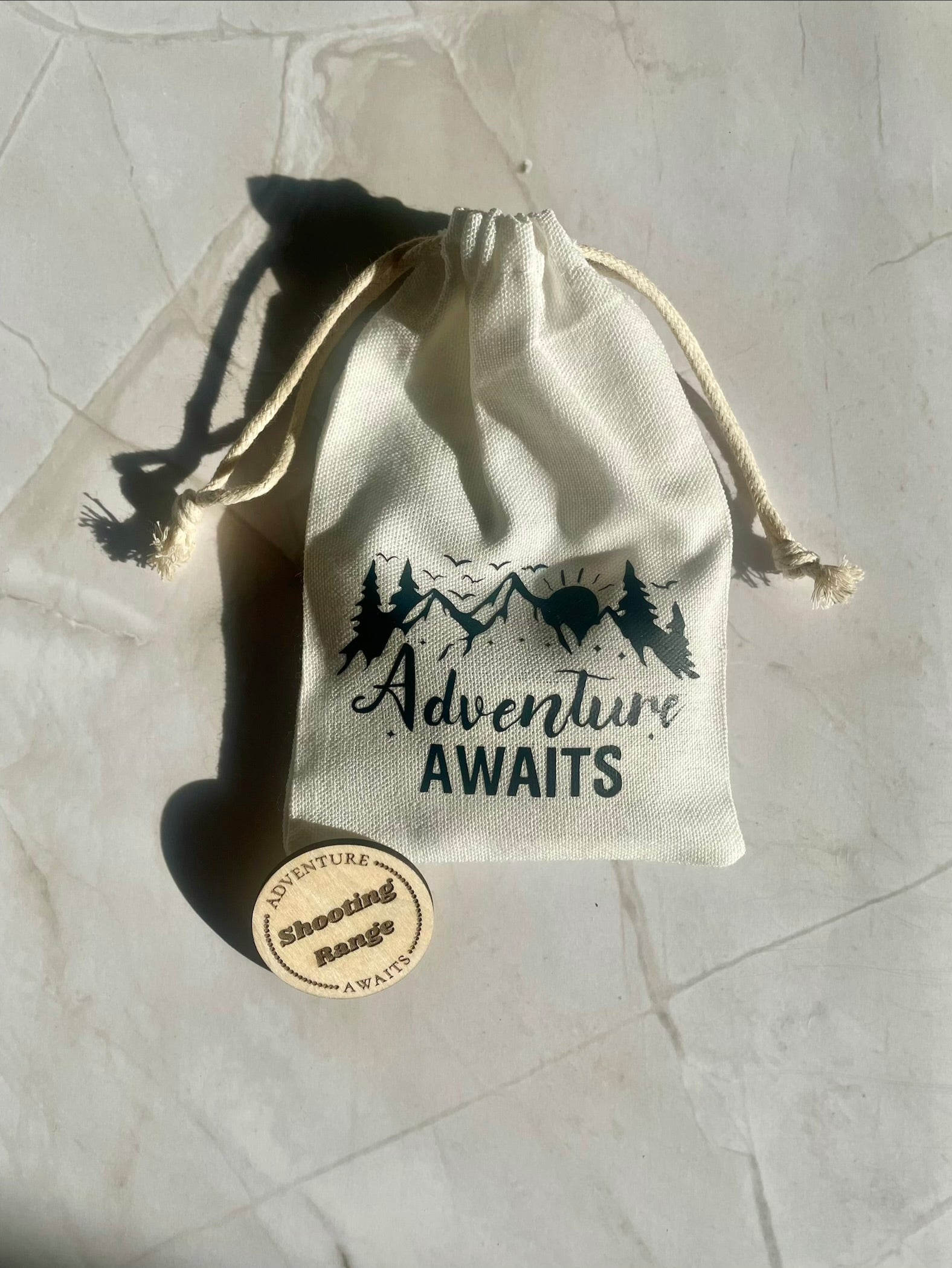 Drawstring bag with 'Adventure Awaits' text on a light marble surface