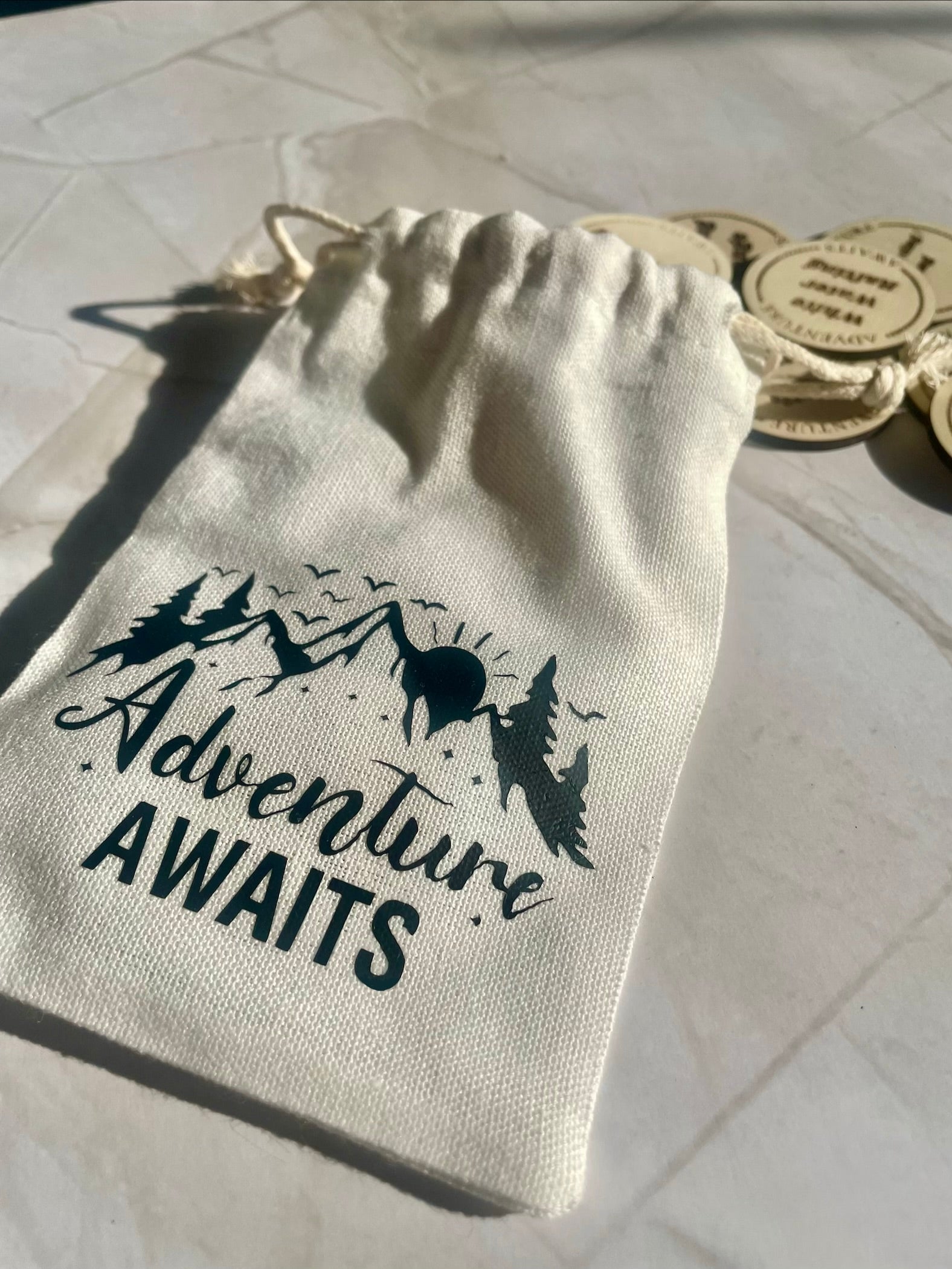 Drawstring bag with 'Adventure Awaits' text and mountain design on a light background