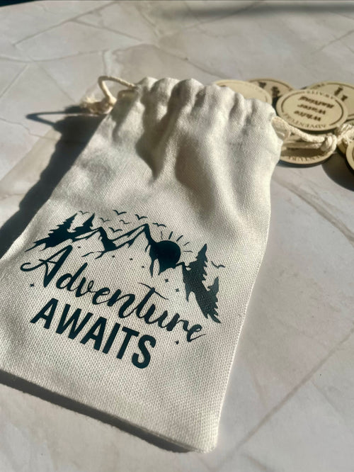Drawstring bag with 'Adventure Awaits' text and mountain design on a light background