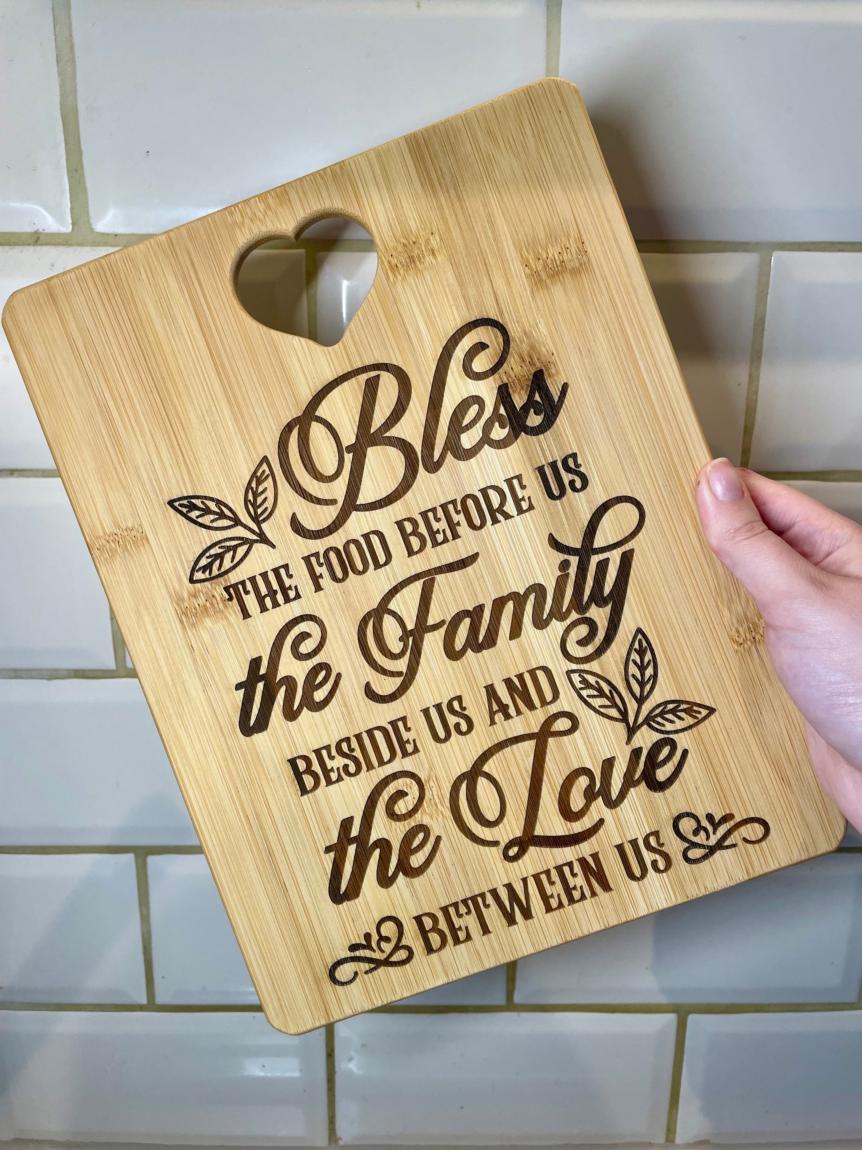 Bamboo cutting board with engraved text held by a hand on a tiled kitchen wall.