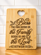 Rectangular bamboo chopping board with engraved family blessing quote and heart handle against white tiled wall