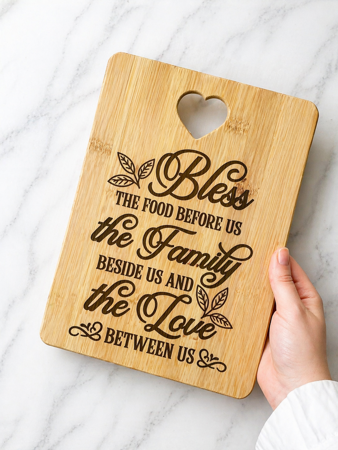Hand holding bamboo chopping board engraved with “Bless the food before us the family beside us and the love between us” quote on marble background