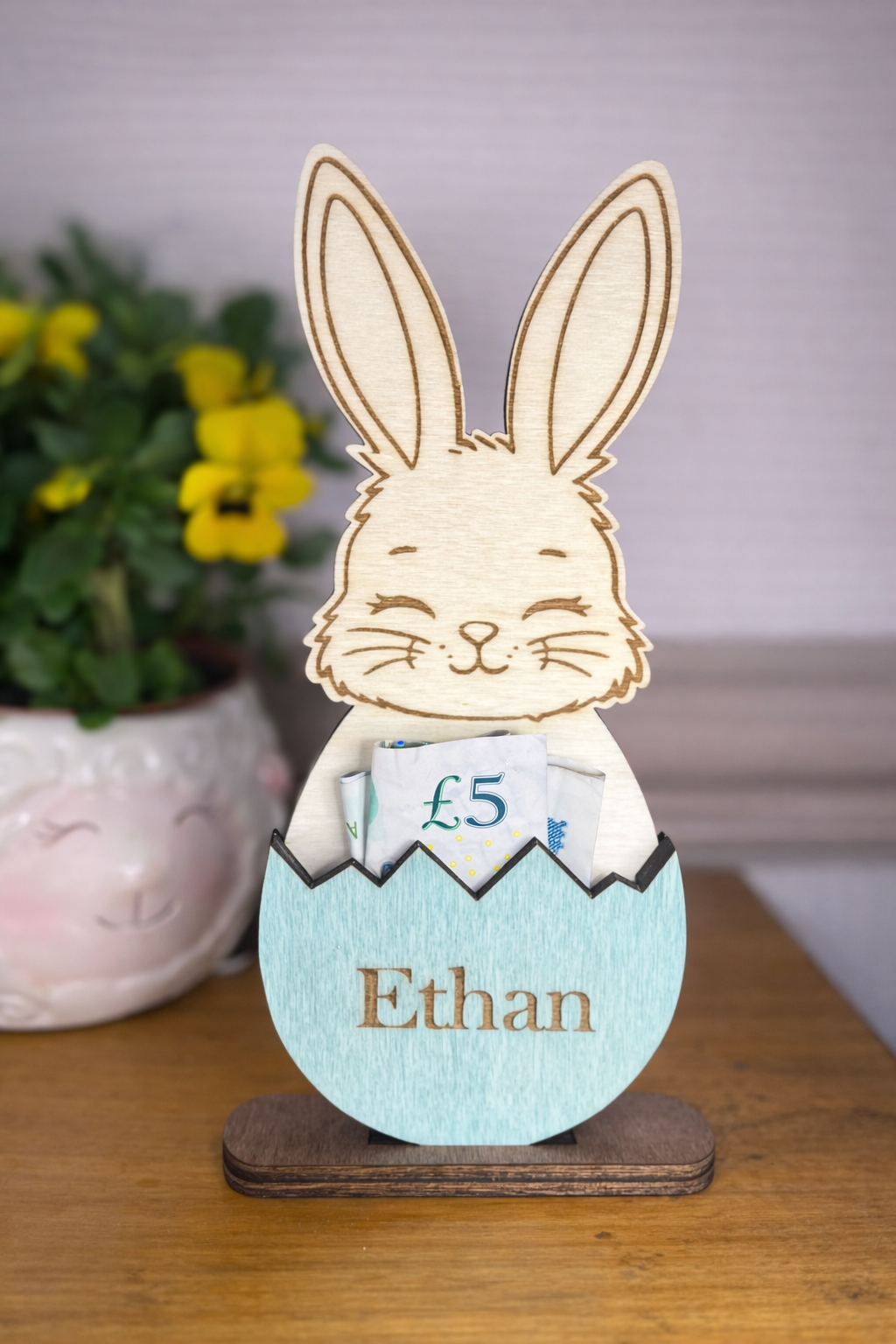Wooden rabbit figure with a hatched egg containing a £5 note, the gg is stained blue and has a personalised name on it