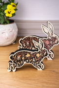 Wooden decorative rabbits beginning to jump. Layered cut outs of florals are inside the bunny silhouette. There is one small bunny stained different shades of brown, and one large bunny stained shades of pastel red/ pink.