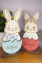 Two wooden rabbit money holders with nameplates 'Ethan' and 'Eleanor' on a wooden surface.