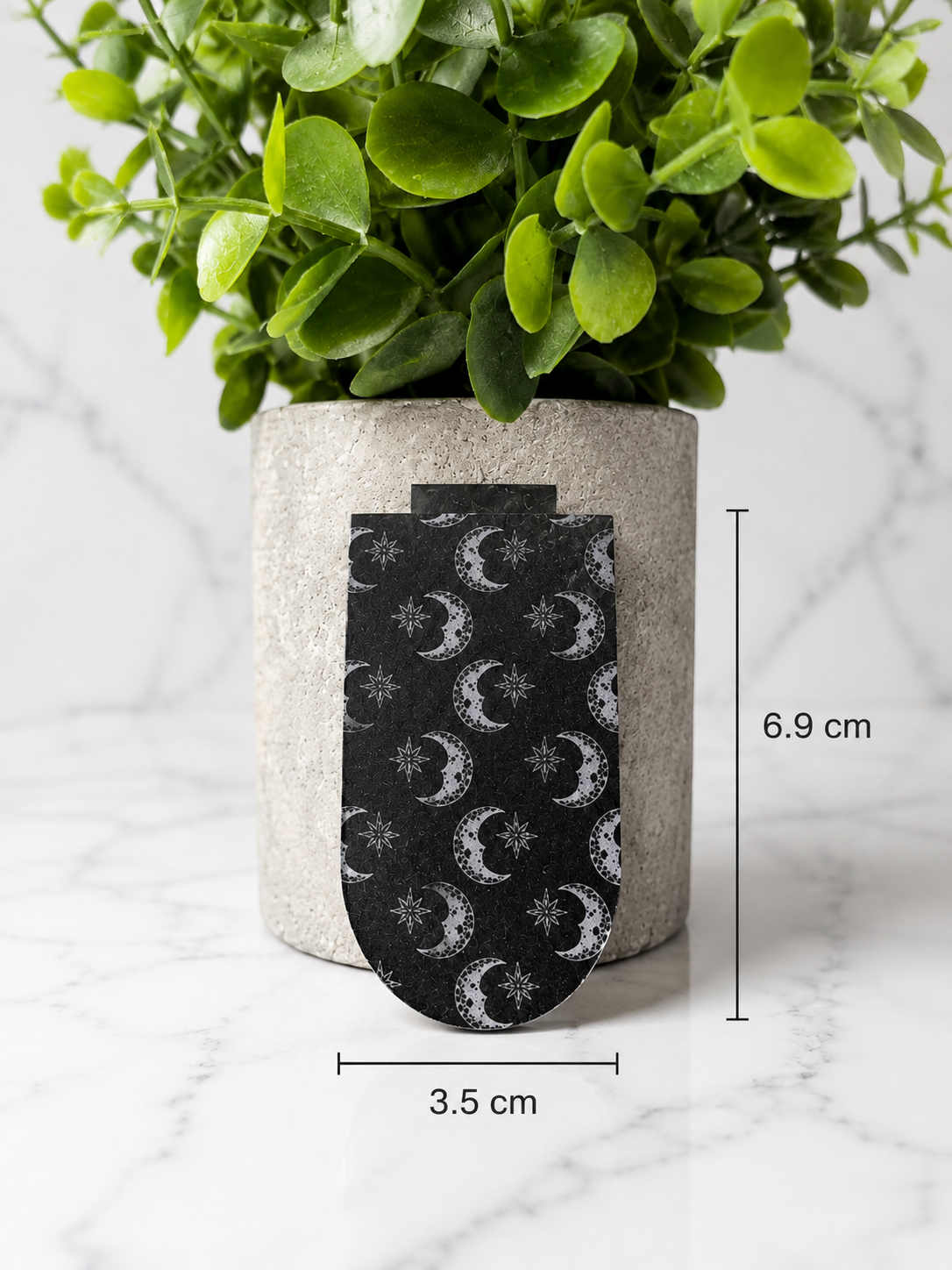 Black magnetic bookmark with moon and star pattern shown with measurements 6.9 cm by 3.5 cm
