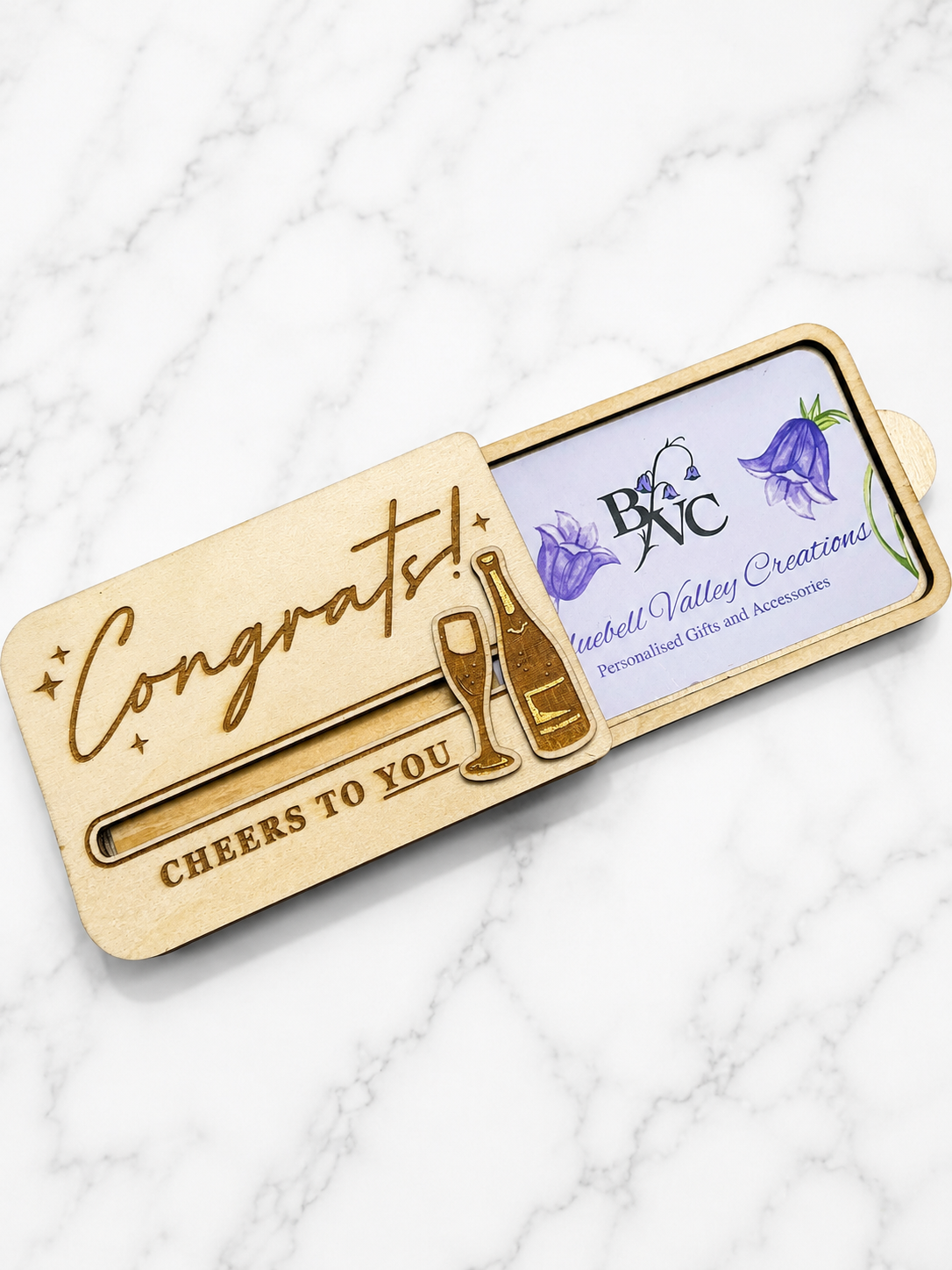 Close up of engraved champagne bottle and glass detail on wooden congratulations gift card holder
