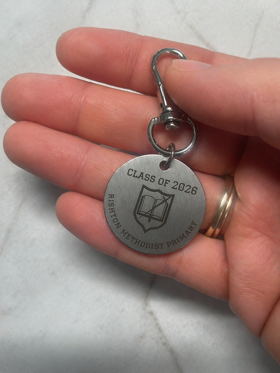 Close-up of engraved Class of 2026 metal keychain held in hand showing school crest design