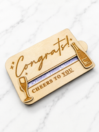 Wooden card with 'Congrats!' and 'Cheers to You' text on a marble surface