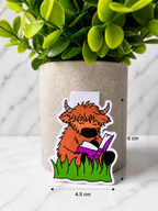 Highland cow magnetic bookmark shaped design holding a book, shown with measurements 6 cm by 4.5 cm against a neutral plant background