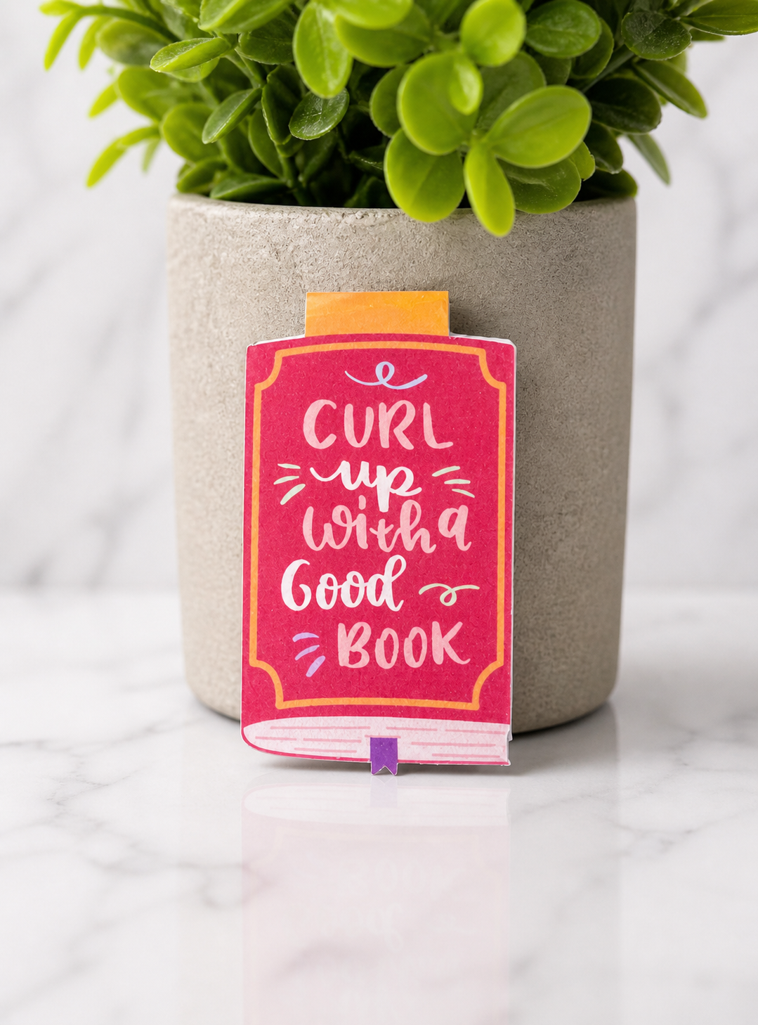 Pink magnetic bookmark with curl up with a good book quote on plant background
