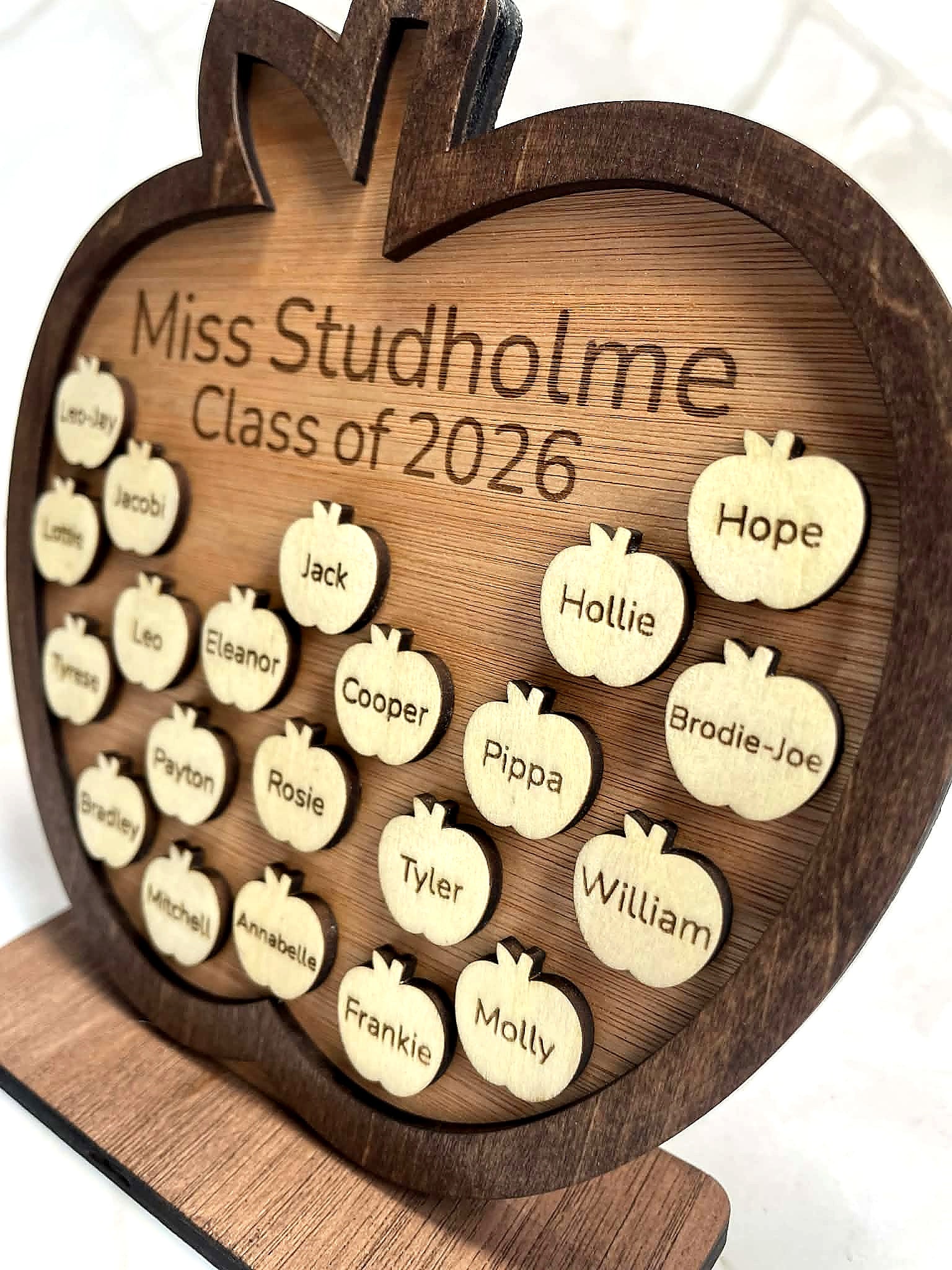 Detailed angled view of engraved wooden apple plaque showing student name pieces and teacher name engraving