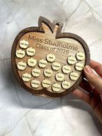 Close-up of personalised wooden apple plaque held in hand, engraved with teacher name and student names
