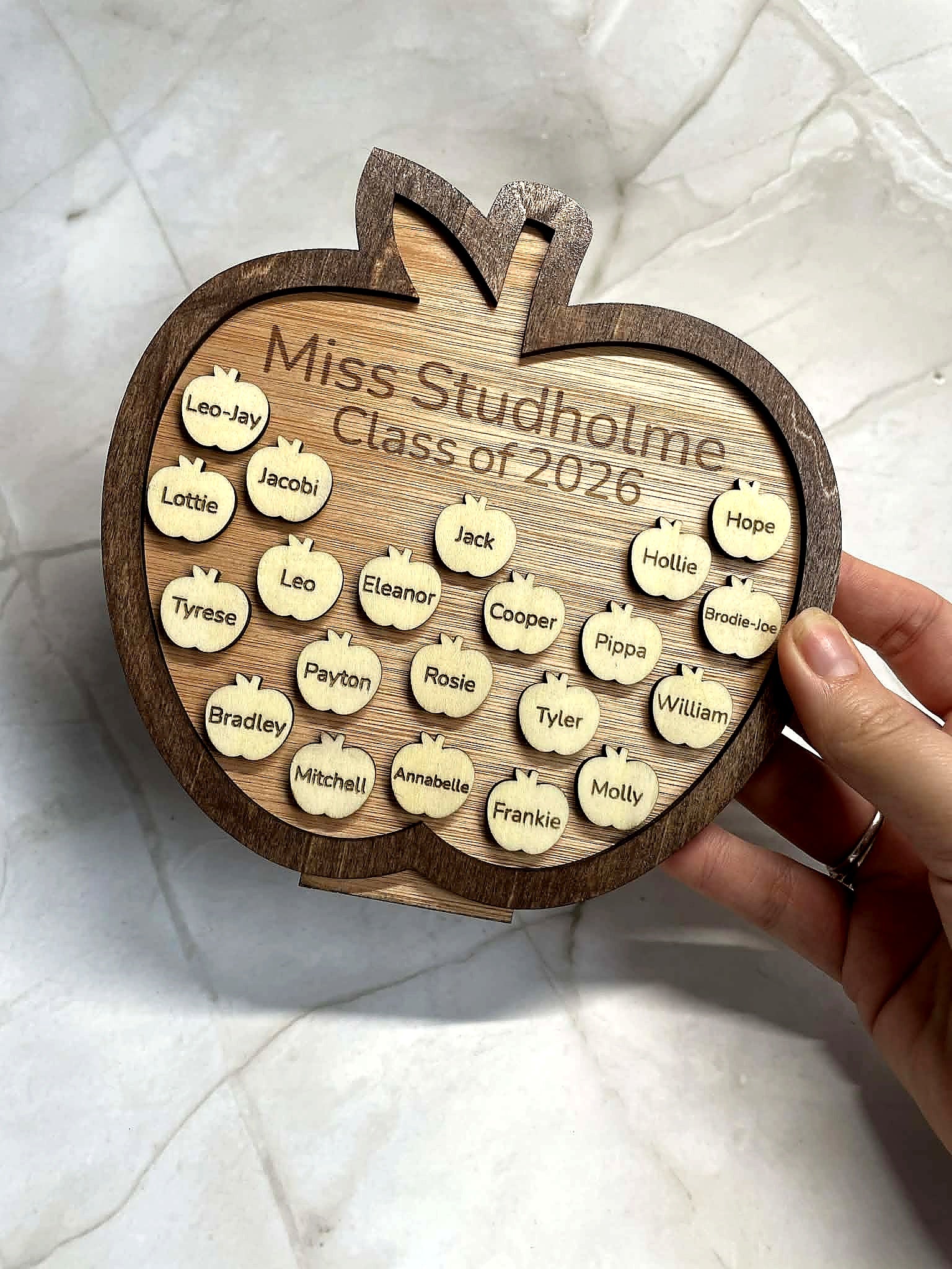 Close-up of personalised wooden apple plaque held in hand, engraved with teacher name and student names