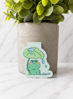 Adorable kawaii style frog magnetic bookmark featuring a green frog with pink cheeks sitting under a leaf umbrella, designed as a cute reading accessory for book lovers