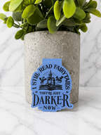 Blue magnetic bookmark with “I still read fairytales they’re just darker now” quote displayed in front of plant