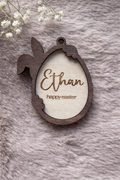 Wooden Easter tag with a bunny holding an egg. the outline is stained dark oak. Written inside the egg are 'Ethan' and 'Happy Easter'.