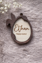 Wooden Easter tag with a bunny holding an egg. the outline is stained dark oak. Written inside the egg are 'Ethan' and 'Happy Easter'.
