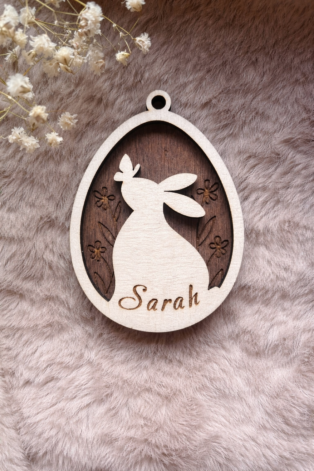 Wooden tag with a bunny and butterfly inside an egg with floral background stained dark oak. on the bottom is space for a personalised name.