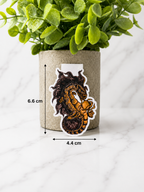 Magnetic bookmark with dragon and astronaut design shown with measurements 6.6 cm by 4.4 cm