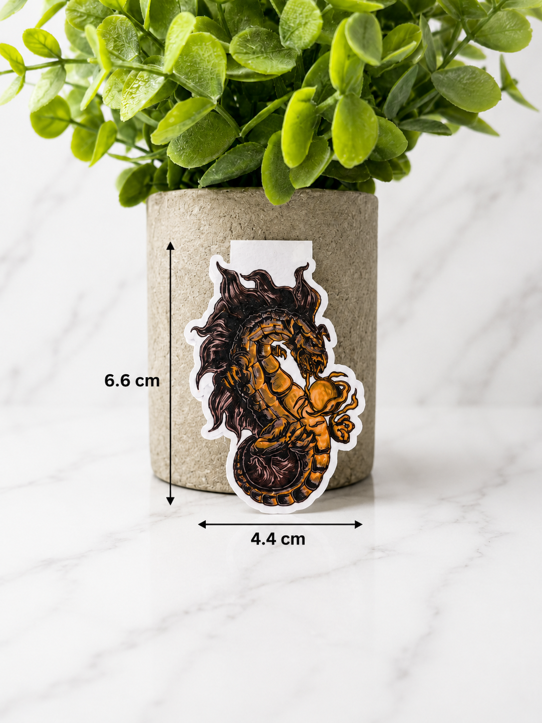 Magnetic bookmark with dragon and astronaut design shown with measurements 6.6 cm by 4.4 cm