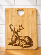 rectangular bamboo chopping board with engraved deer and fawn design and heart handle against white tiled wall