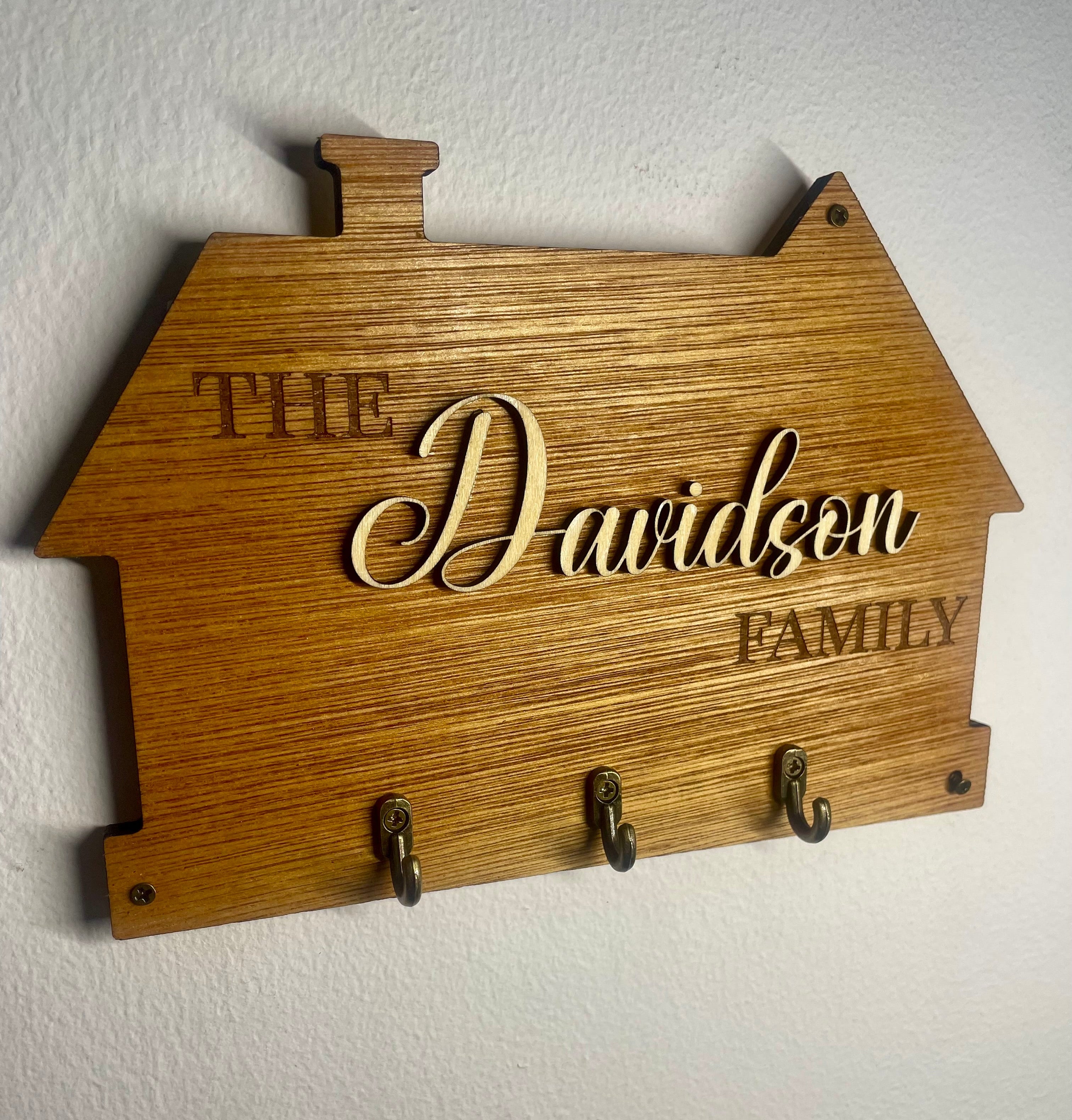 Wooden house-shaped plaque with 'The Davidson Family' engraving on a white wall.