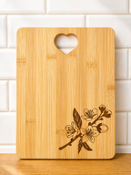 Rectangular bamboo chopping board with engraved floral corner design and heart handle against white tiled wall