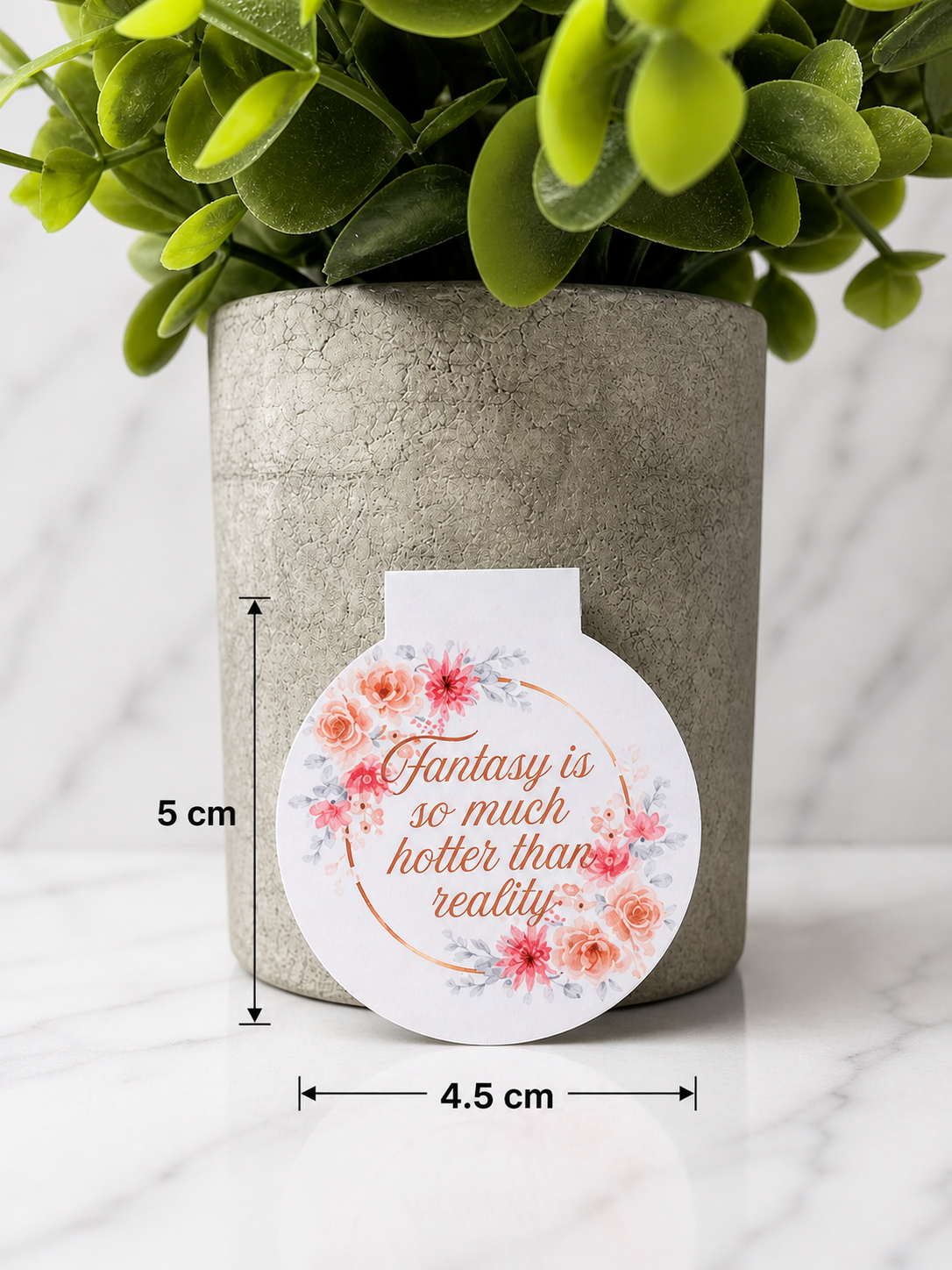 Round floral magnetic bookmark with romantic quote “Fantasy is so much hotter than reality” shown with measurements of approximately 5 cm tall and 4.5 cm wide against a neutral background