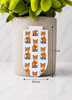 Magnetic bookmark with repeating fox design shown with measurements 7 cm by 3.6 cm on a marble background with plant