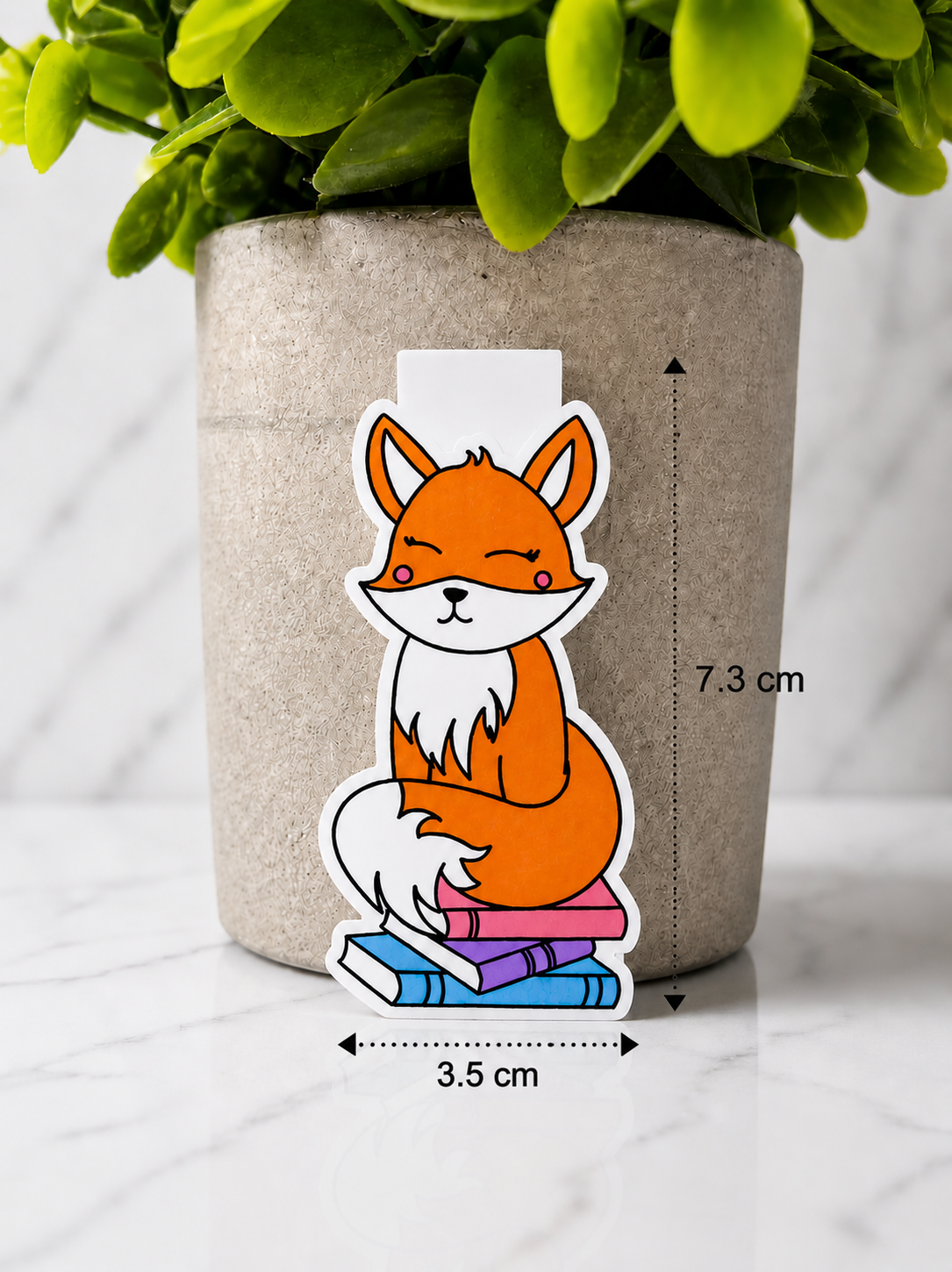 Magnetic bookmark featuring a cute orange fox sitting on books with measurements 7.3 cm by 3.5 cm against a neutral background