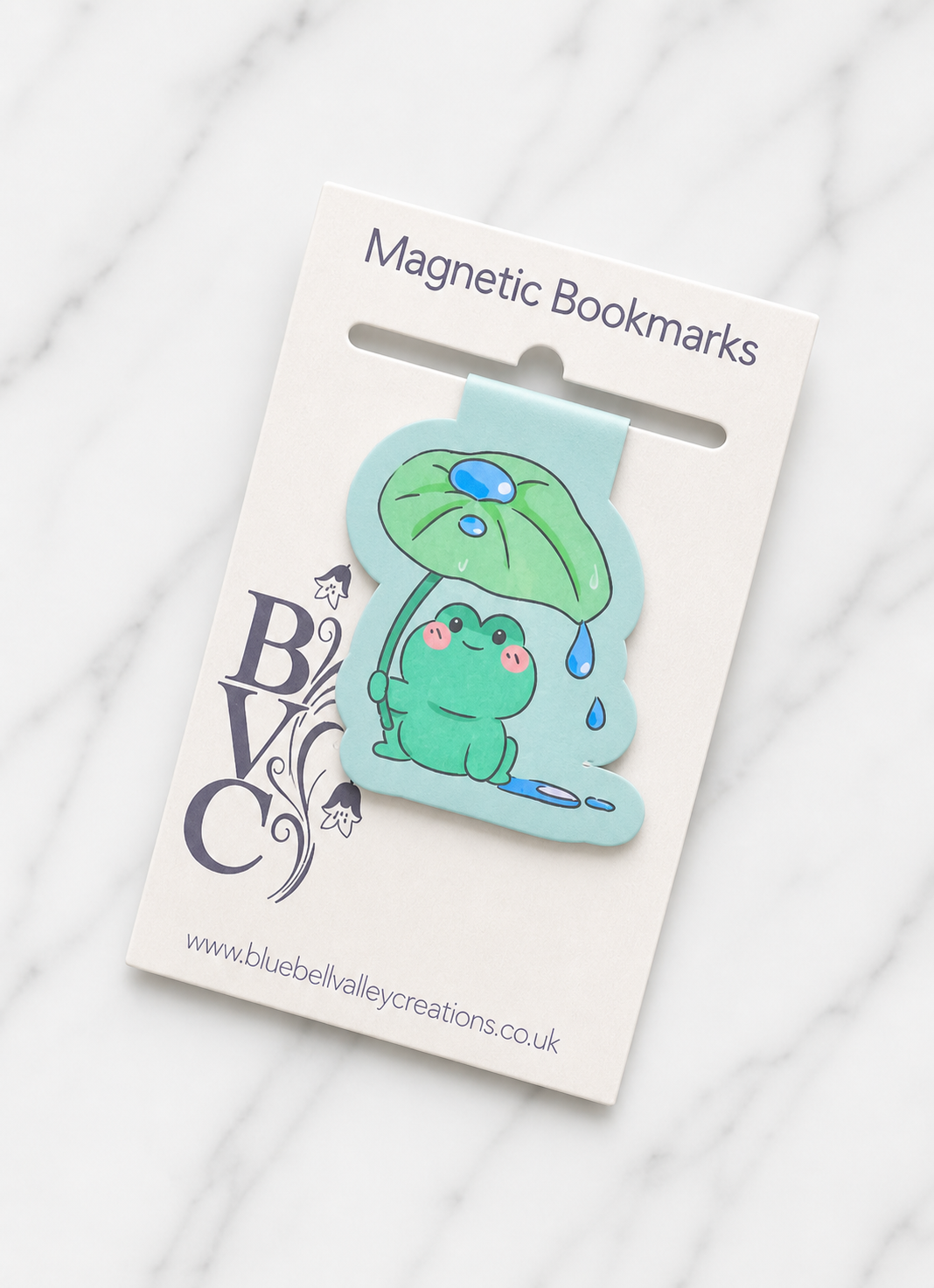 Cute frog magnetic bookmark attached to branded backing card packaging, showing how the bookmark is presented as a gift-ready item for readers and stationery lovers