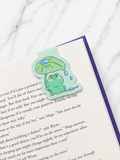 Small frog magnetic bookmark placed at the top of a book page, showing how the magnetic design grips both sides of the page to mark reading progress