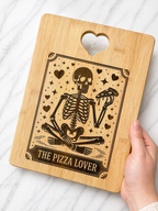 Hand holding bamboo chopping board engraved with skeleton holding pizza slice and “The Pizza Lover” text on marble background