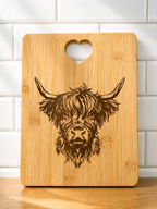 Square bamboo chopping board engraved with detailed Highland cow design and heart handle against tiled kitchen wall