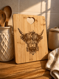 Engraved bamboo chopping board with Highland cow design styled in warm kitchen setting with utensils and soft lighting