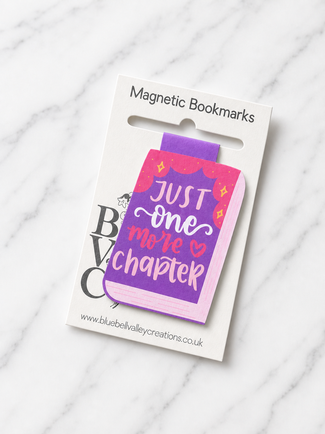 Magnetic bookmark shaped like a book with the phrase “Just one more chapter” in purple and pink, displayed on Bluebell Valley Creations branded packaging against a white marble background