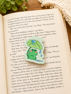 Cute frog magnetic bookmark resting on an open book in a cosy reading setting, with soft lighting and warm textures creating a relaxing aesthetic for book lovers