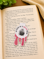 Dark romance skeleton magnetic bookmark resting on an open book in a cosy reading setup with warm lighting, greenery and textured fabric background