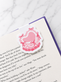 Pink heart magnetic bookmark with bow design clipped onto the top of an open book page, showing how it securely marks pages while reading