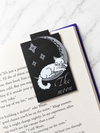 Magnetic bookmark featuring a sleeping cat on a crescent moon used to mark a page in a book