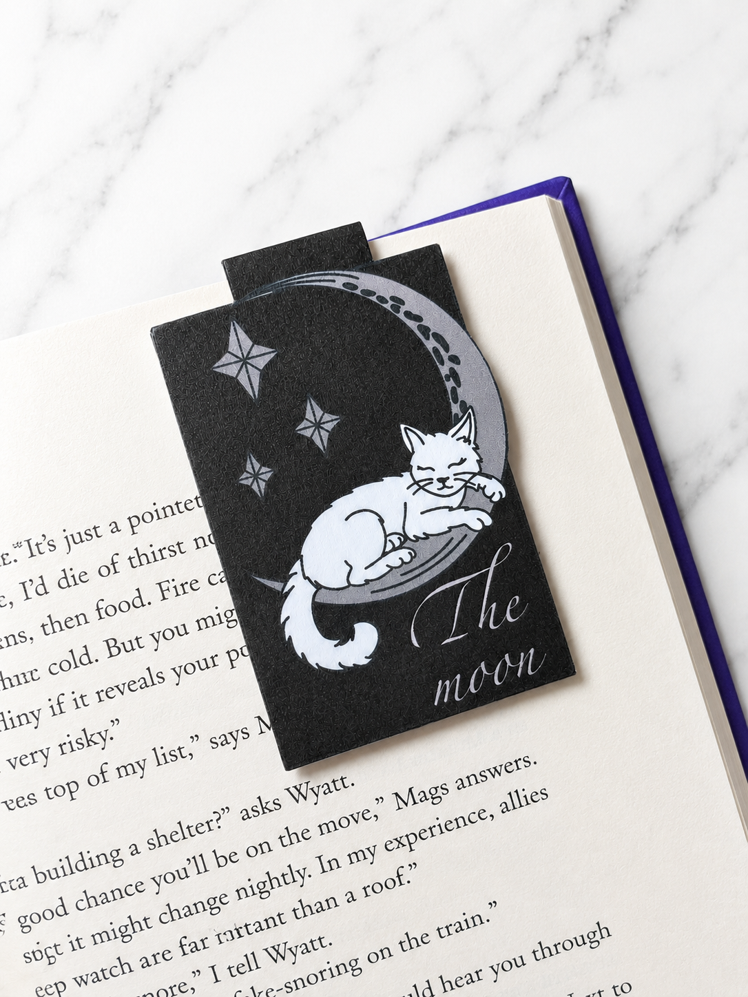Magnetic bookmark featuring a sleeping cat on a crescent moon used to mark a page in a book