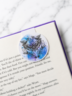 Round magnetic bookmark with moth and crystal design clipped onto a book page