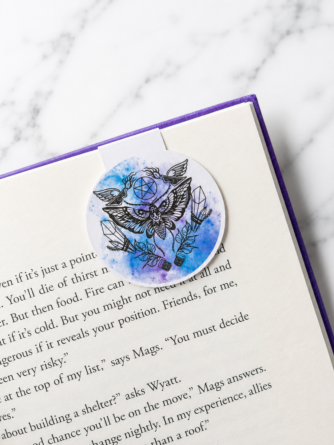 Round magnetic bookmark with moth and crystal design clipped onto a book page