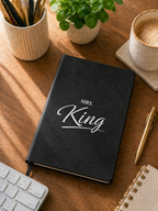 Black notebook with 'Mrs. King' on a wooden desk with office supplies