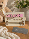 Wooden welcome little one gift card holder displayed with teddy bear and baby gift setting