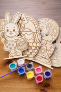 4 Wooden Easter-themed cutouts with paint containers and a brush on a wooden surface