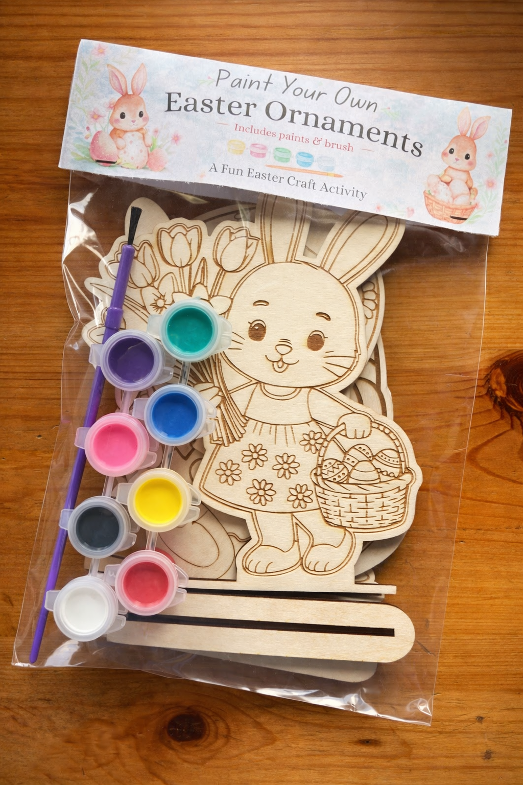 Paint your own Easter ornament kit with wooden cutout, paint, and brush on a wooden surface.