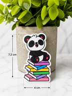 Cute panda magnetic bookmark sitting on colourful stacked books shown with measurements 7.2 cm by 4 cm against a neutral plant background